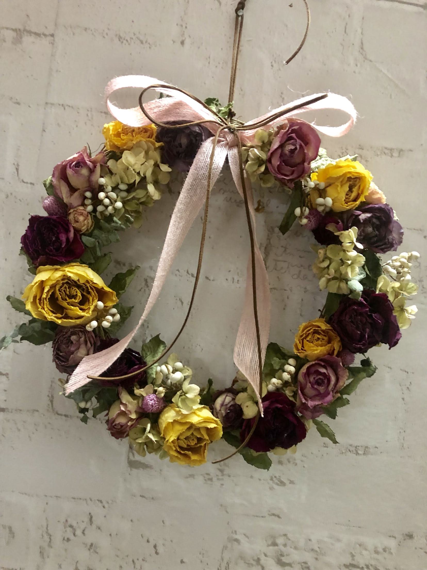Natural Rose Round Garland with pink ribbon and dried flowers in burgundy, yellow, and cream.